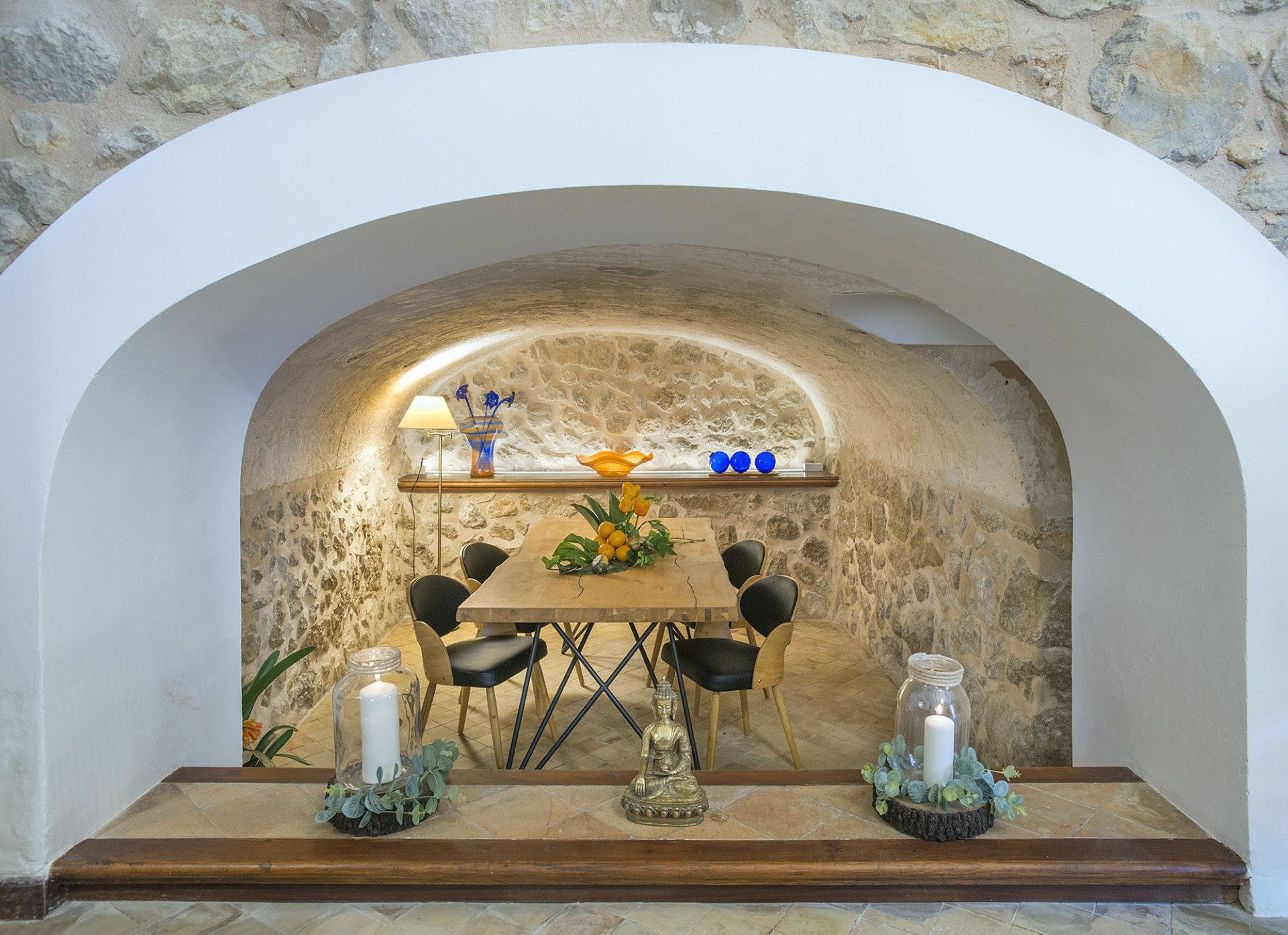 A rustic dining nook with a table, chairs, and decorative items set into a stone alcove.