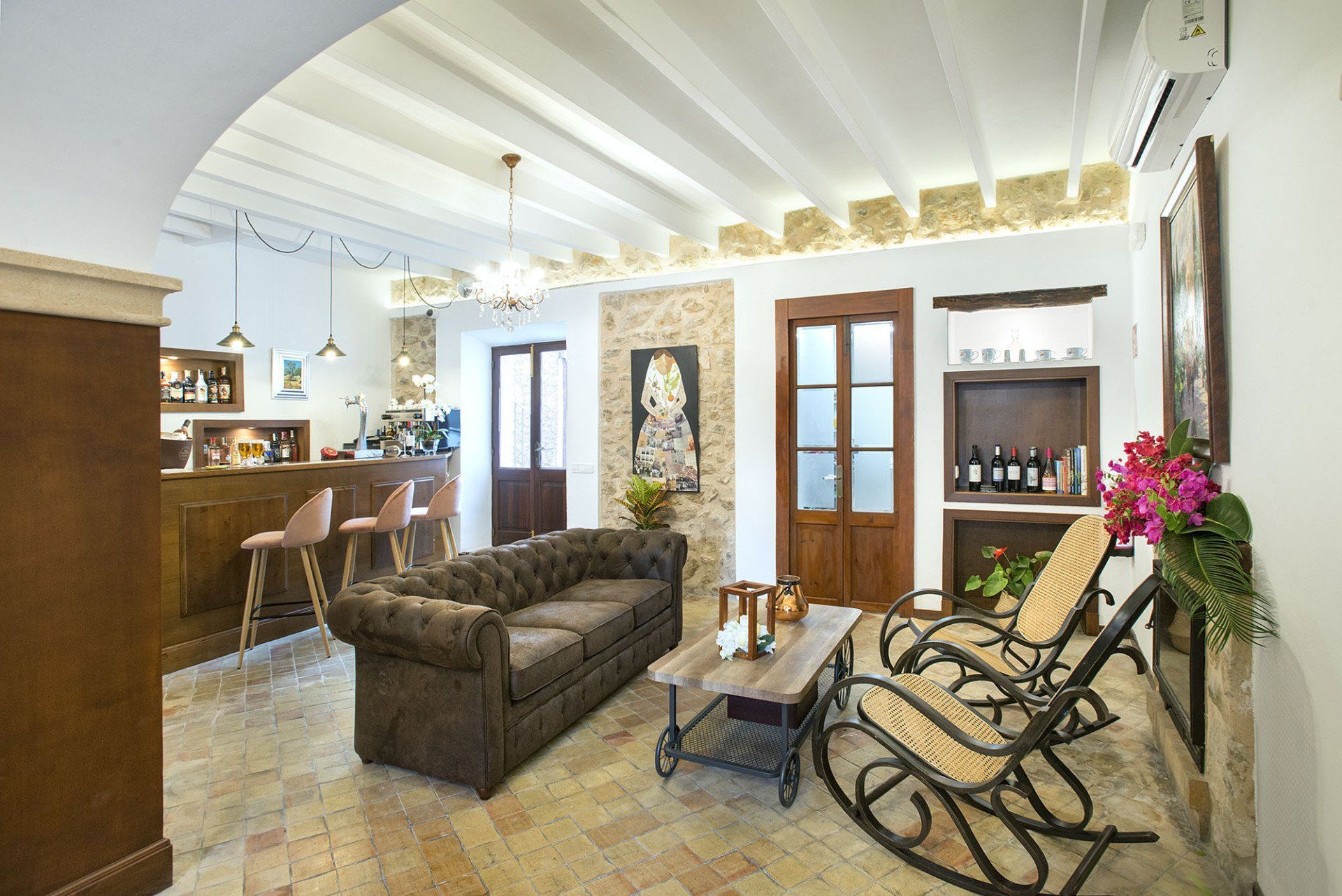 Cozy living room with tufted sofa, rocking chairs, and a bar area, warm tones, stone wall accents.