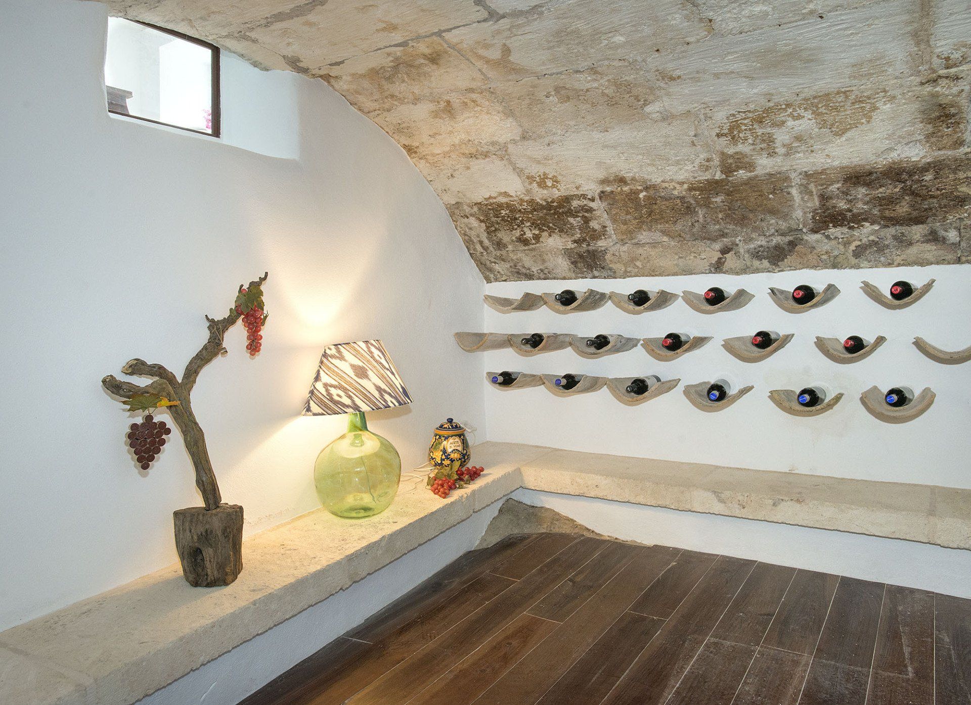 Wine cellar with arched stone ceiling, wooden floor, and bottle storage on the wall.