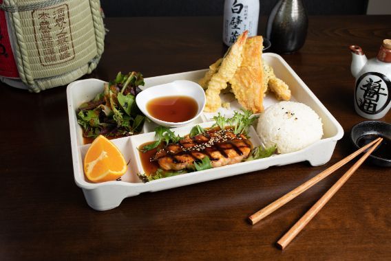 A bento box with variety of food with chopsticks on a wooden table.