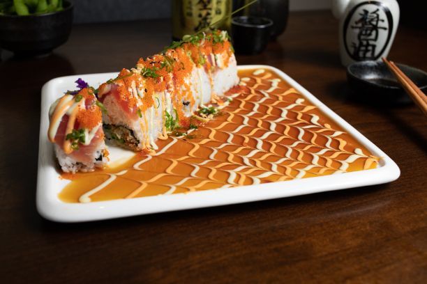 A white plate topped with sushi and sauce( Four Seasons Roll) on a wooden table.