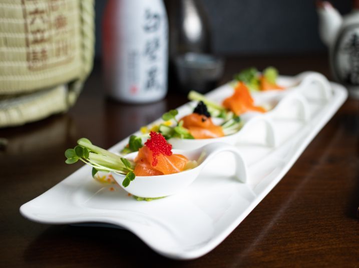 A plate of food ( Fuji salmon) with a bottle of sake in the background.