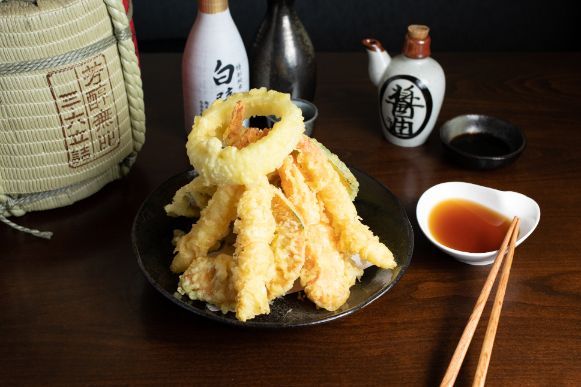 A plate of  Tempura Mix with chopsticks and dipping sauce on a table.
