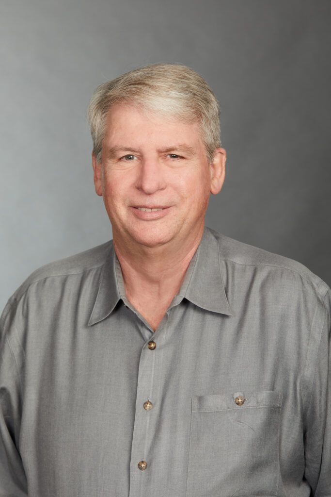 A man in a gray shirt is smiling for the camera.