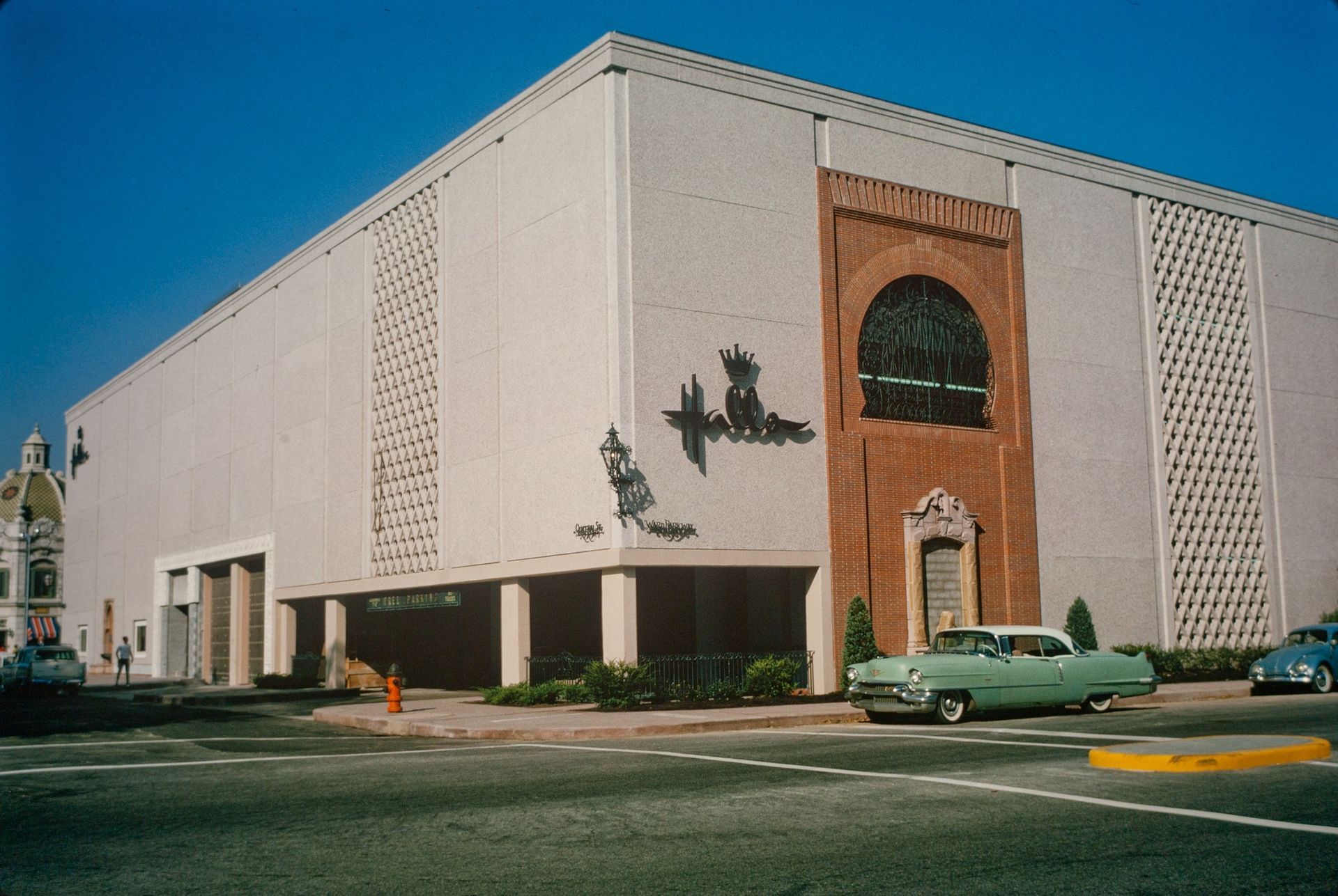 A green car is parked in front of a large building