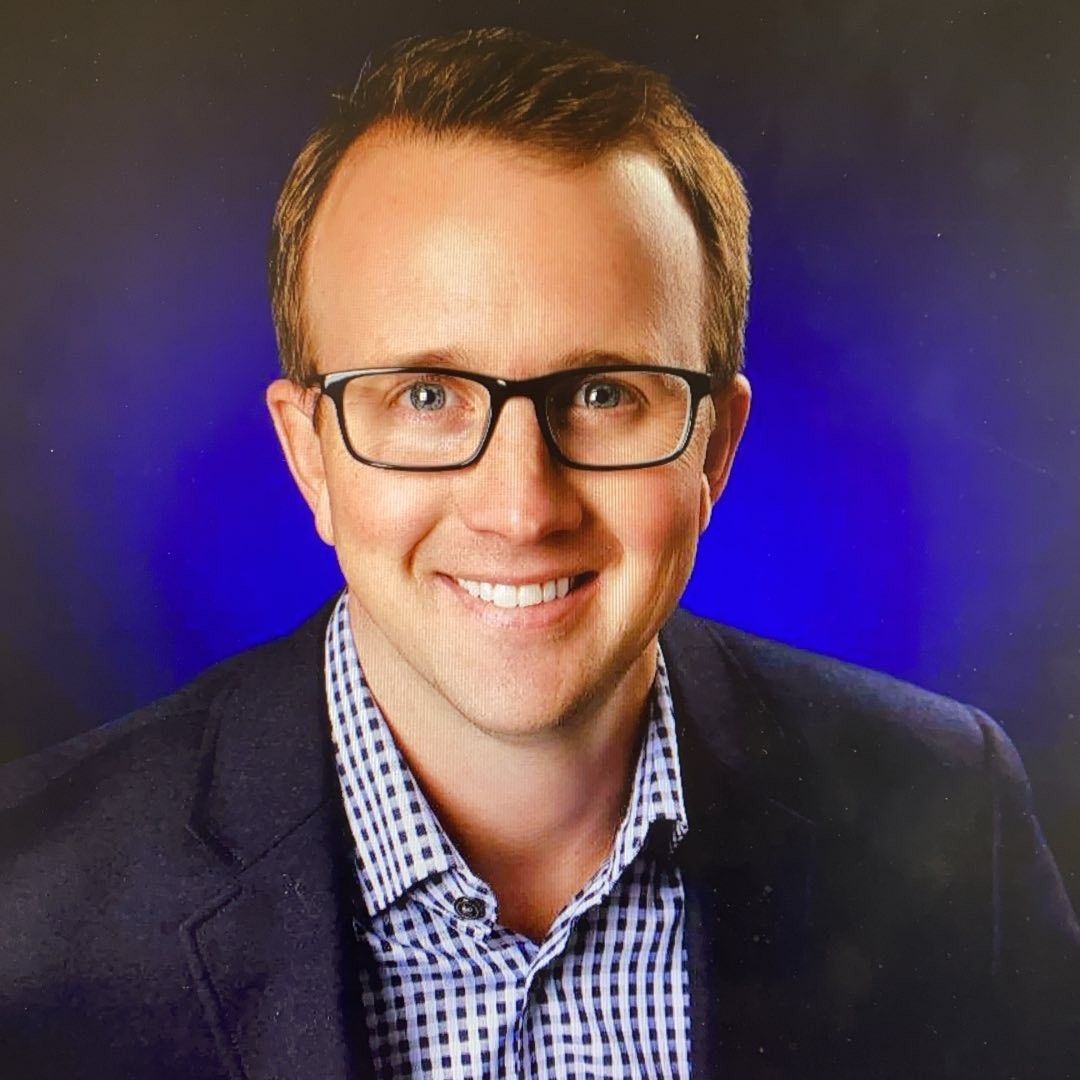 Smiling man in glasses and blazer against a blue studio background