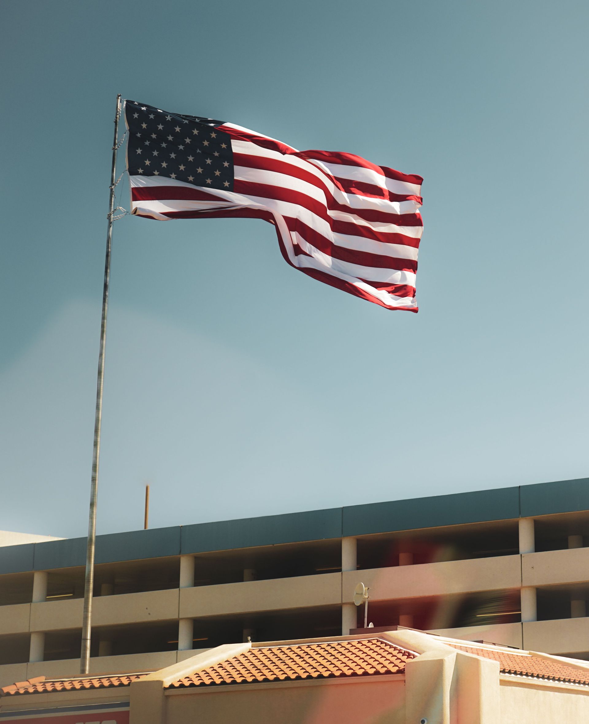 American flag waving on a pole above a building under a clear blue sky