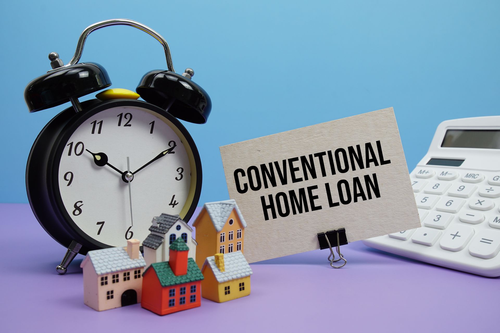 Alarm clock, model houses, and a sign reading “CONVENTIONAL HOME LOAN” beside a calculator.