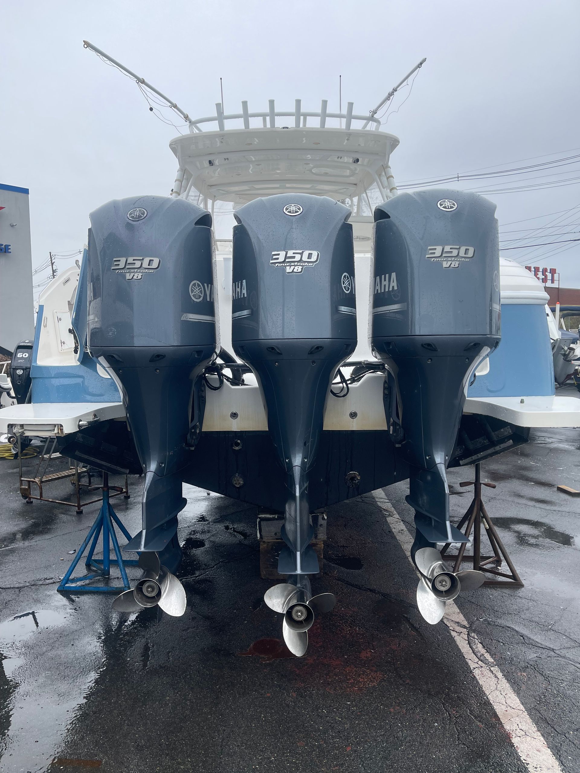 The stern of a white motorboat on jacks, featuring three large dark blue Yamaha outboard motors in a paved lot.