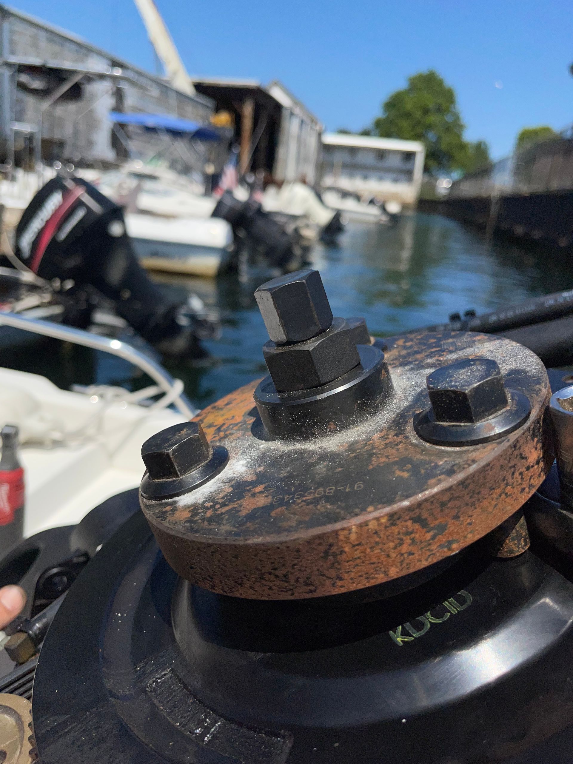 A close-up view of a metal boat propeller hub assembly, with blurred boats and a marina in the background.