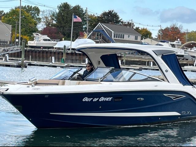A dark blue and white Sea Ray SLX motorboat named "Out of Office" moving through water in a marina.