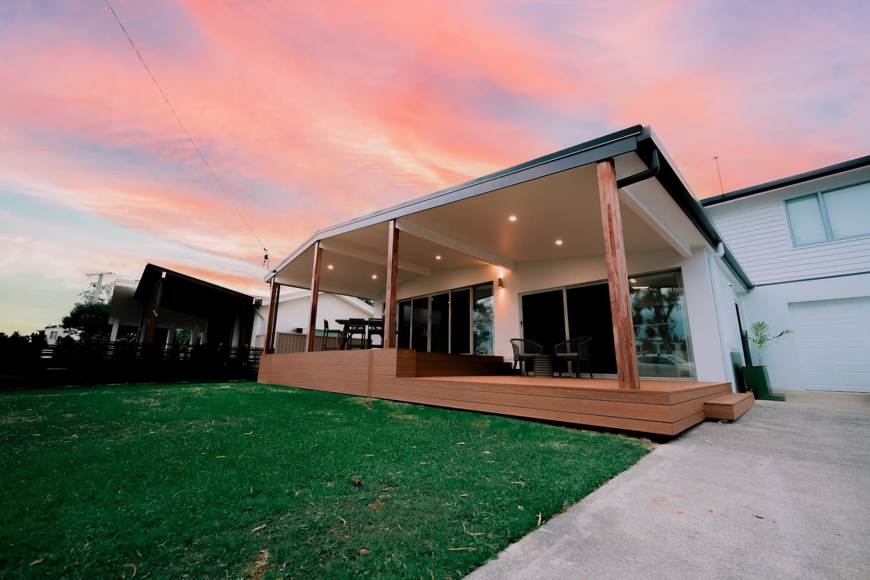 House with deck, under a sunset sky. Lawn in front.