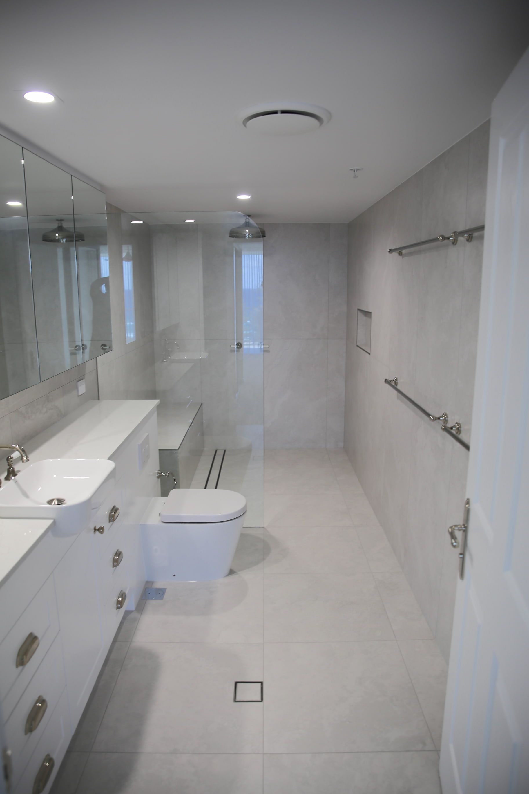 Modern, white bathroom with double vanity, shower, and toilet.