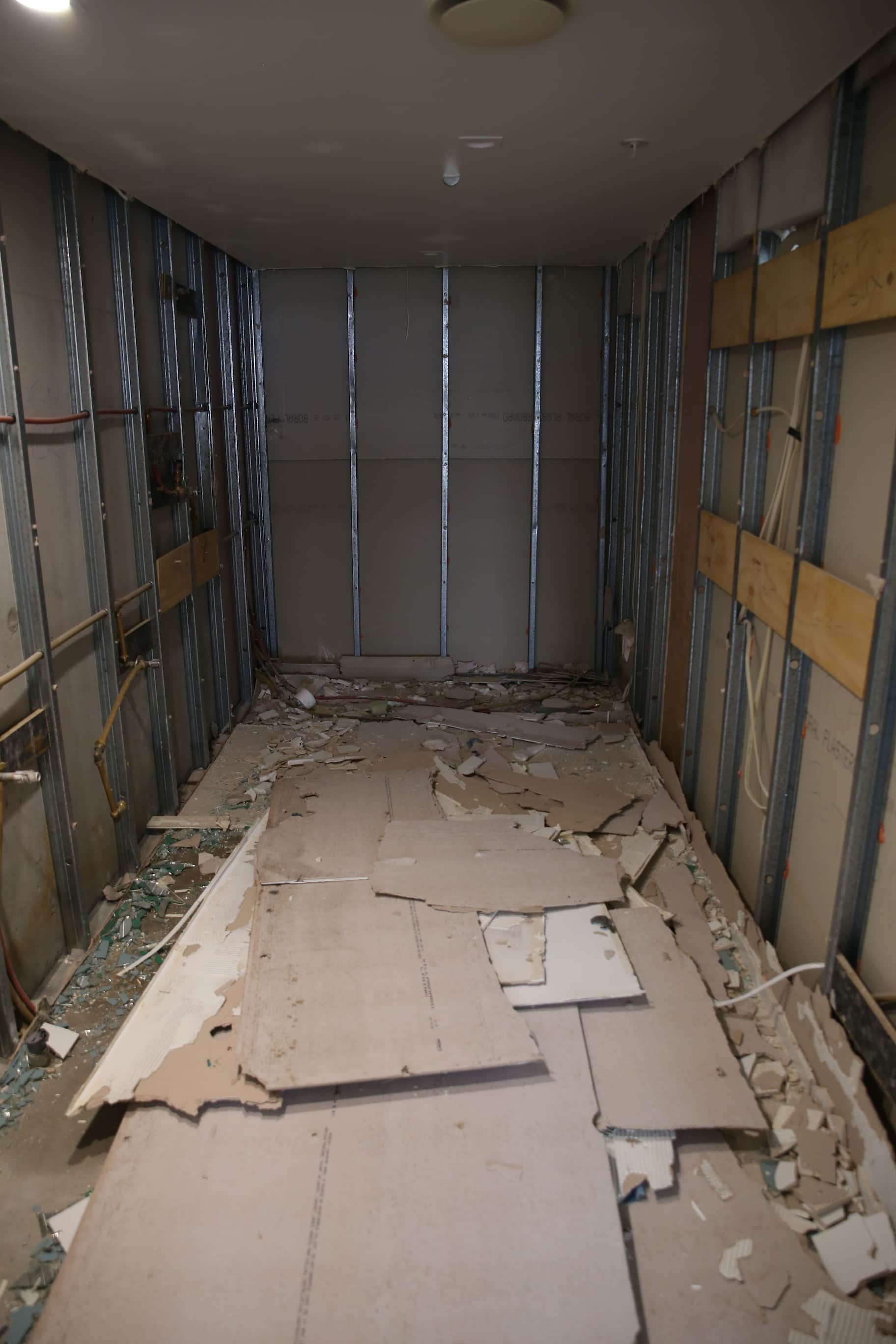 Room under construction: walls gutted, exposed metal studs, debris on the floor, overhead light.