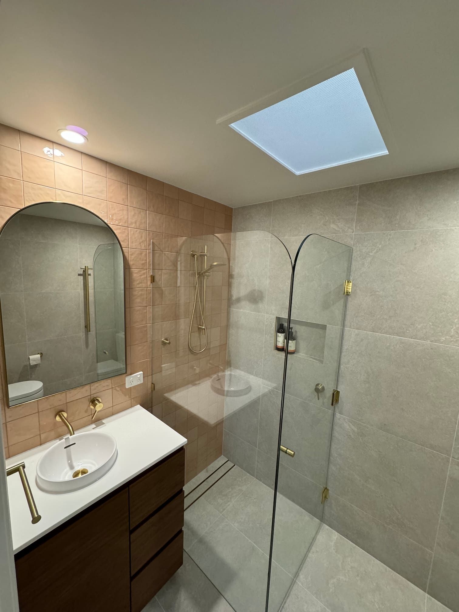 Modern bathroom with a glass shower, gold fixtures, and a skylight.