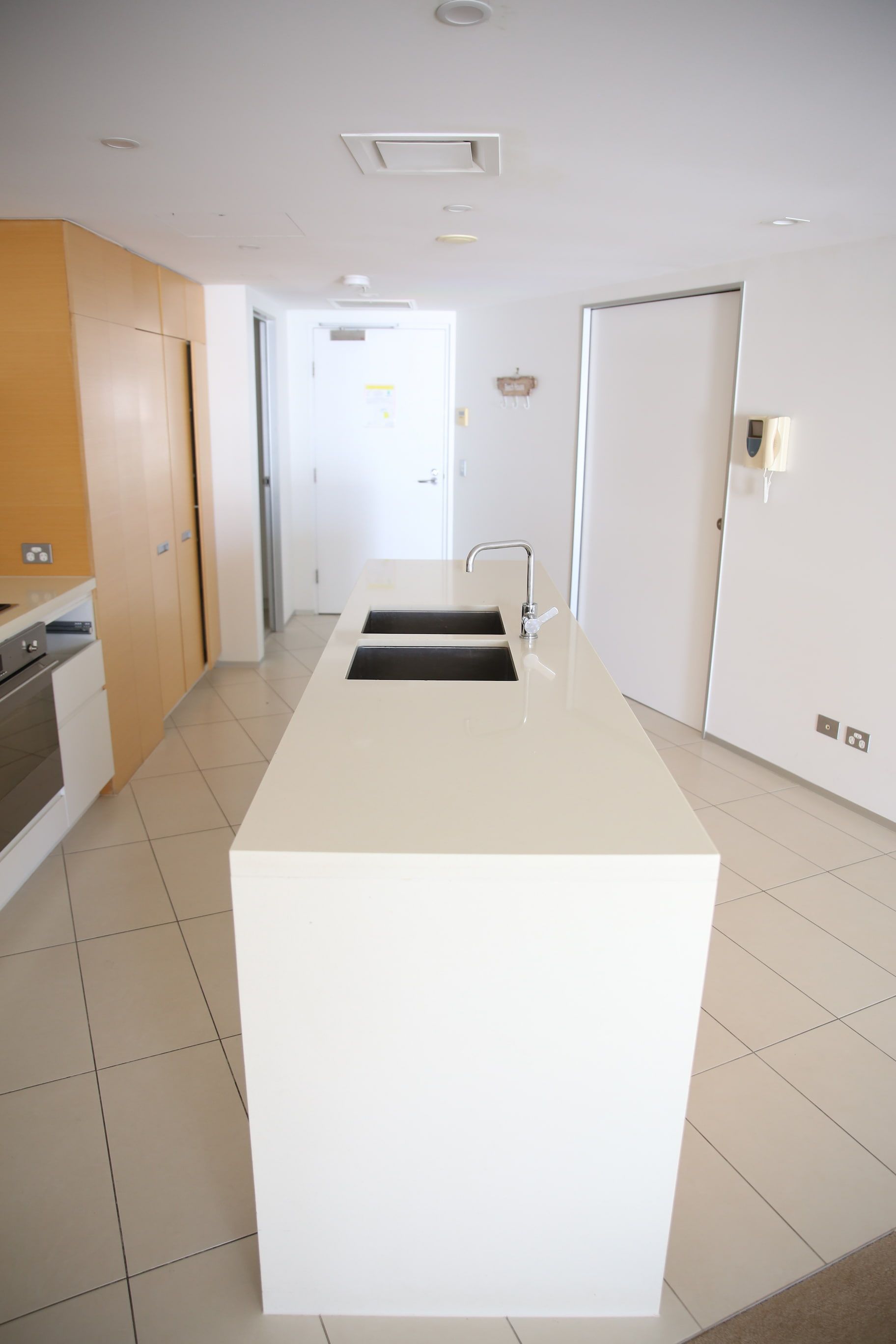 Modern white kitchen with island, stainless steel sink, tile floor, and light wood cabinetry.