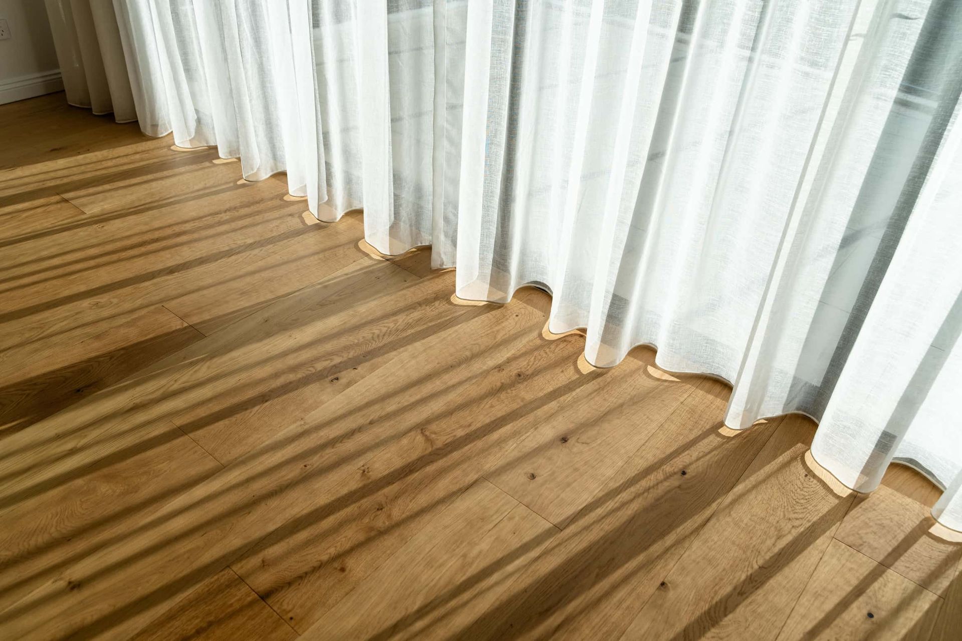Wooden floor with shadows cast by sheer white curtains.