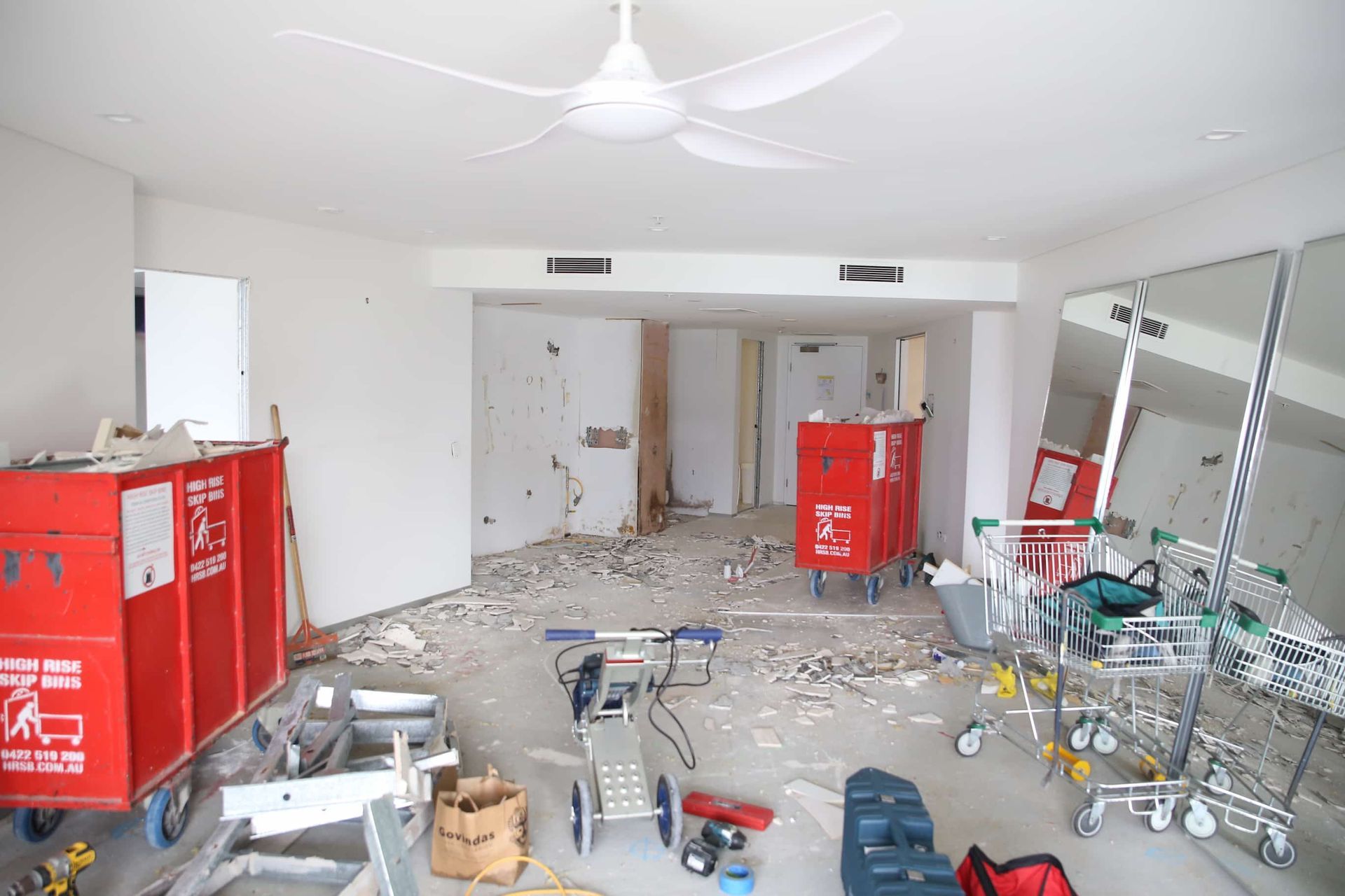 Room under renovation, construction debris on floor, red bins, and a ceiling fan.