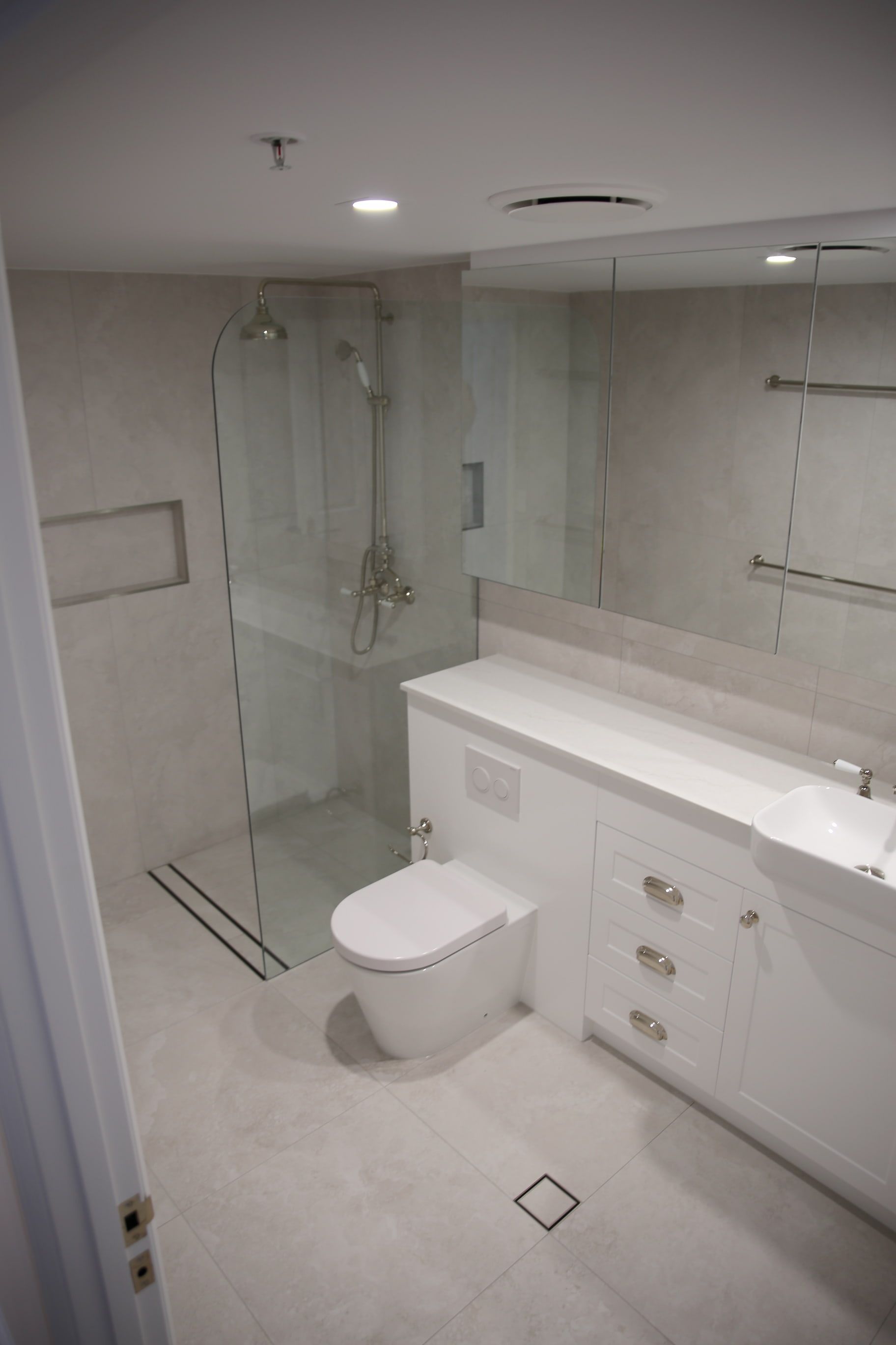 Modern bathroom with white cabinets, toilet, glass shower, and large mirror.