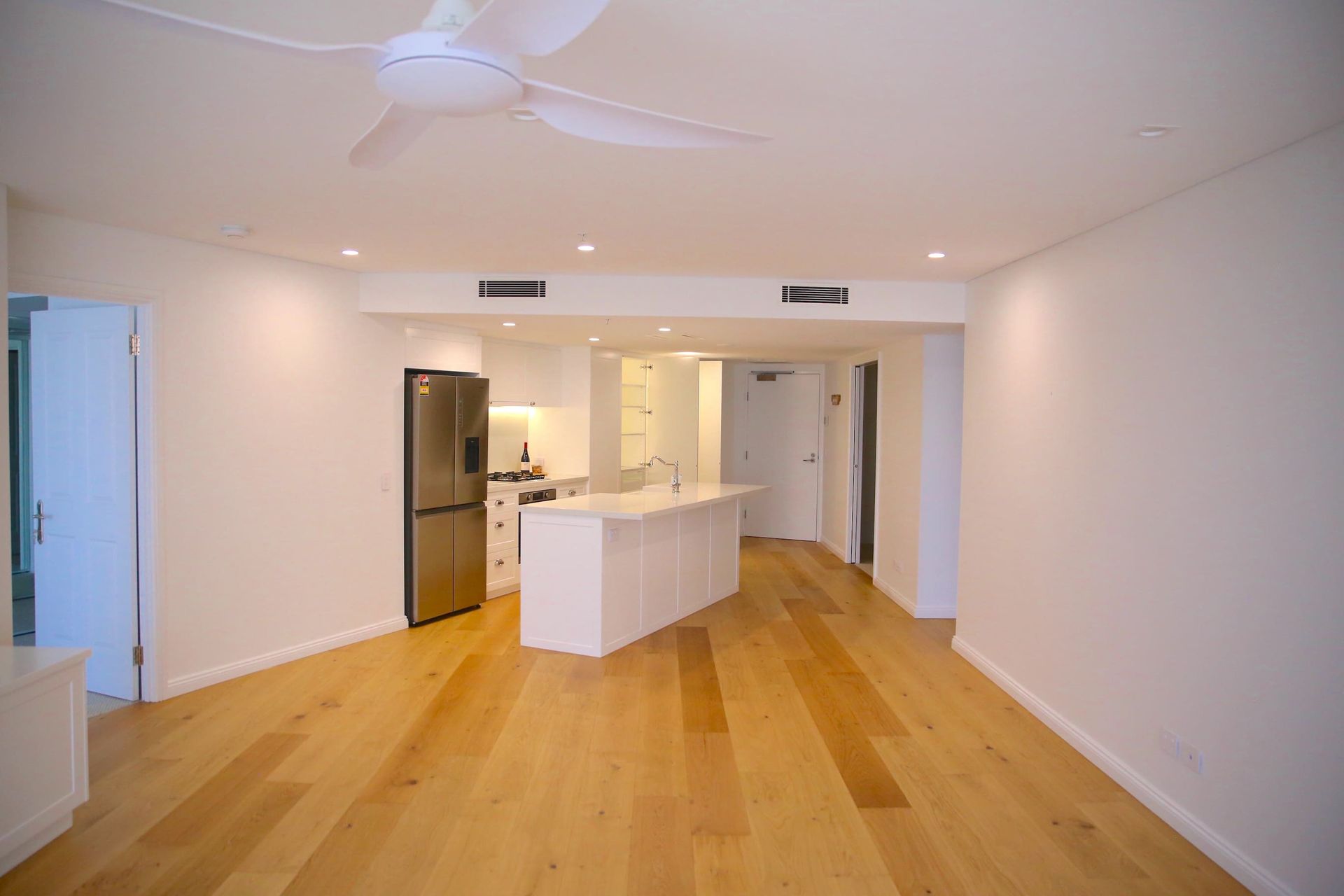 Empty apartment interior with hardwood floors, kitchen island, and ceiling fan.
