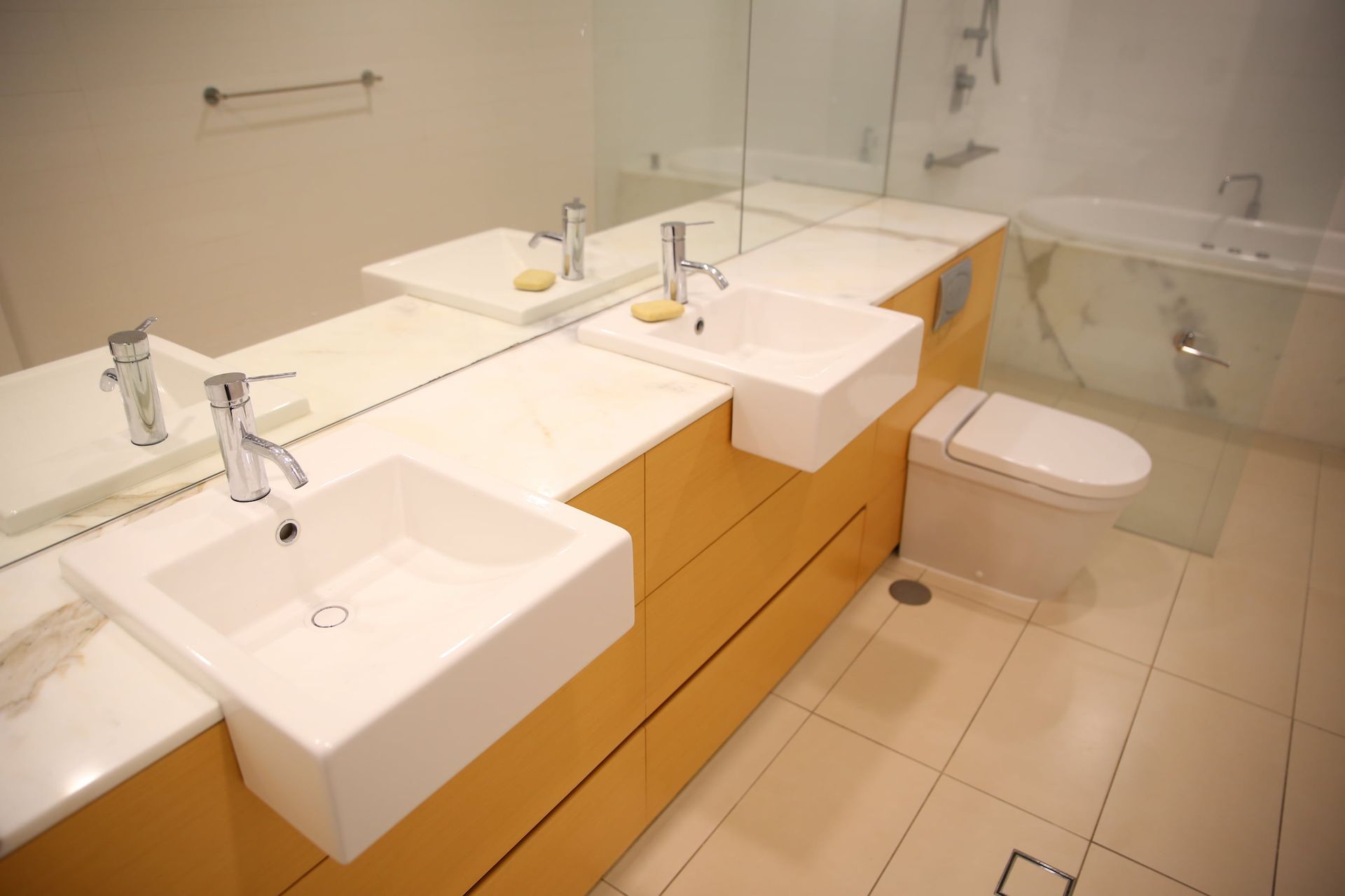 Modern bathroom with two sinks, a toilet, and a bathtub; beige and white colors.