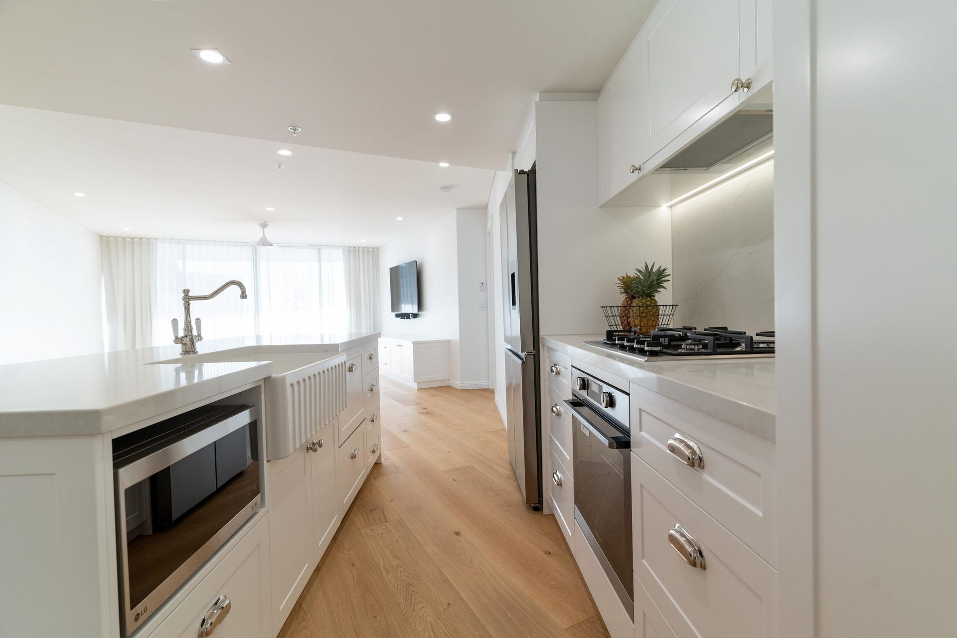 White kitchen with island, stainless steel appliances, and wood flooring.
