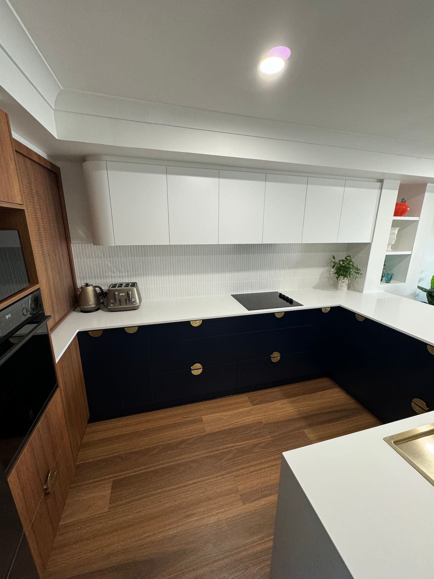 Modern kitchen with dark blue and white cabinetry, white countertops, and wood flooring.