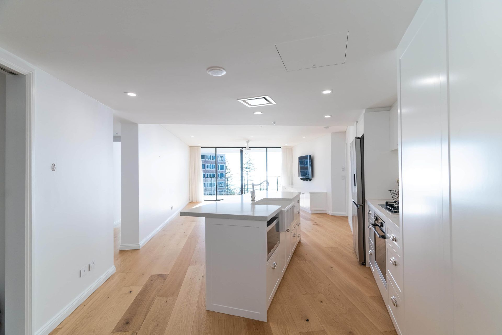 Modern white kitchen with island, wood floors, and city view from window.