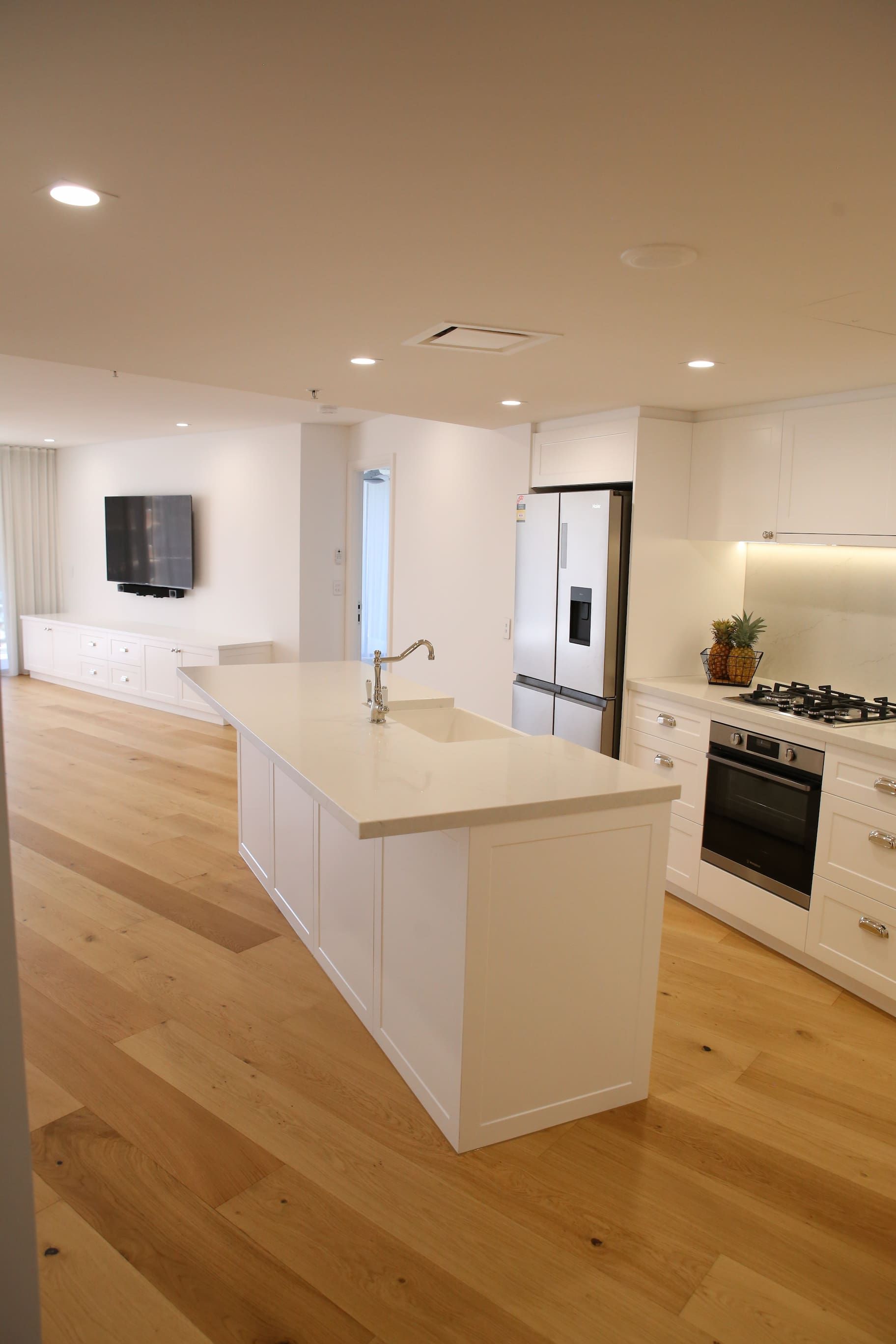 Spacious white kitchen with light wood floors, an island with a sink, and stainless steel appliances.