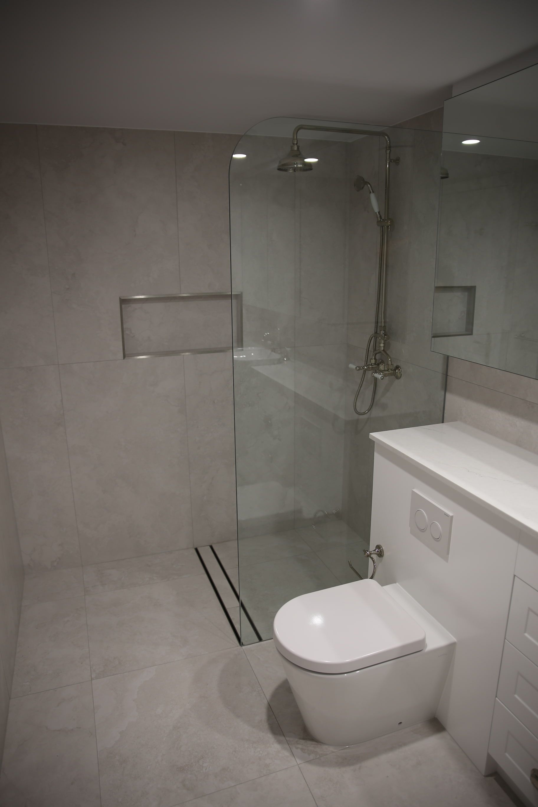 Modern bathroom with a glass shower, white toilet, and marble-like tile.