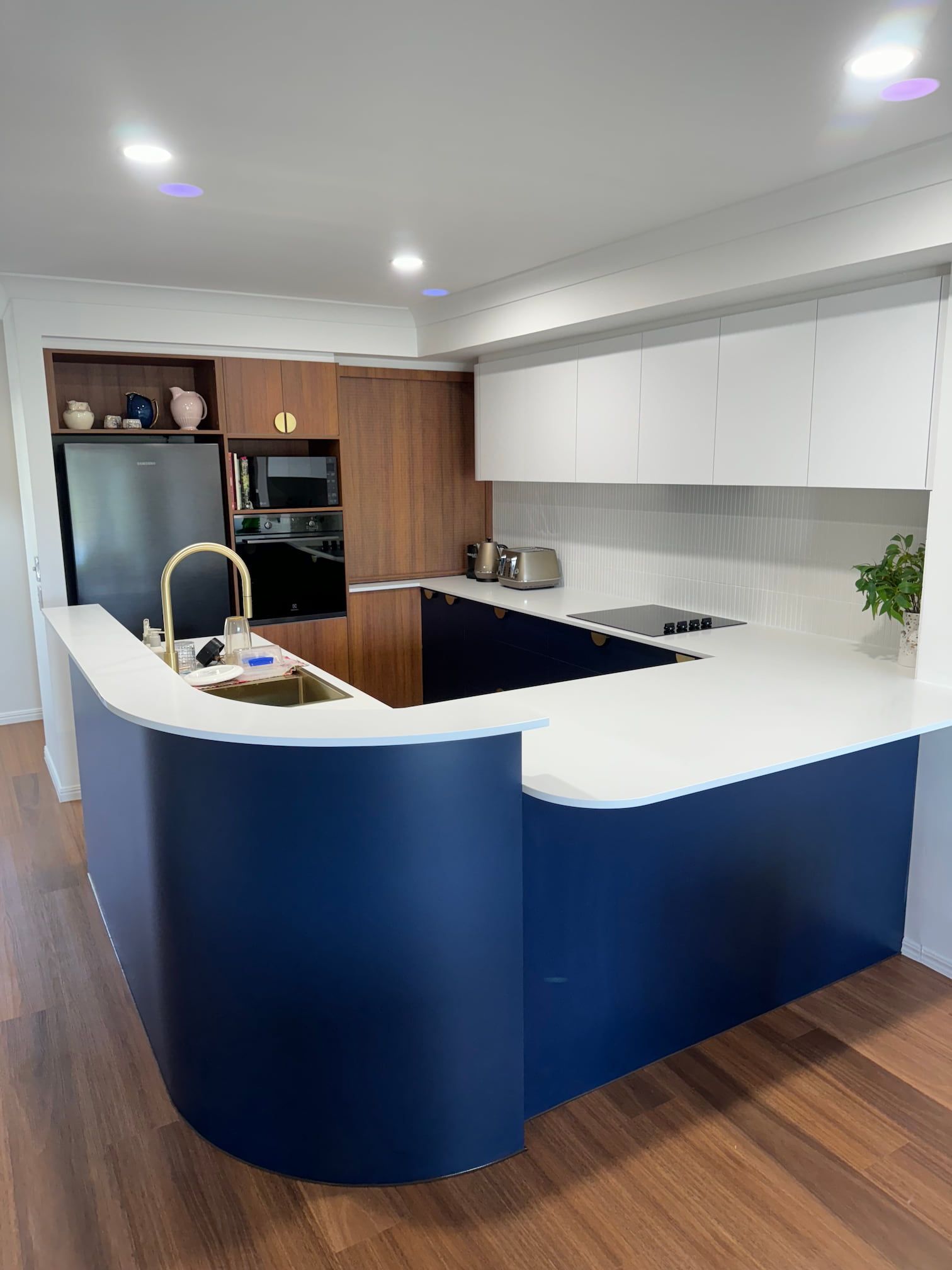Modern kitchen with dark blue curved island, white countertops, and wood cabinetry.