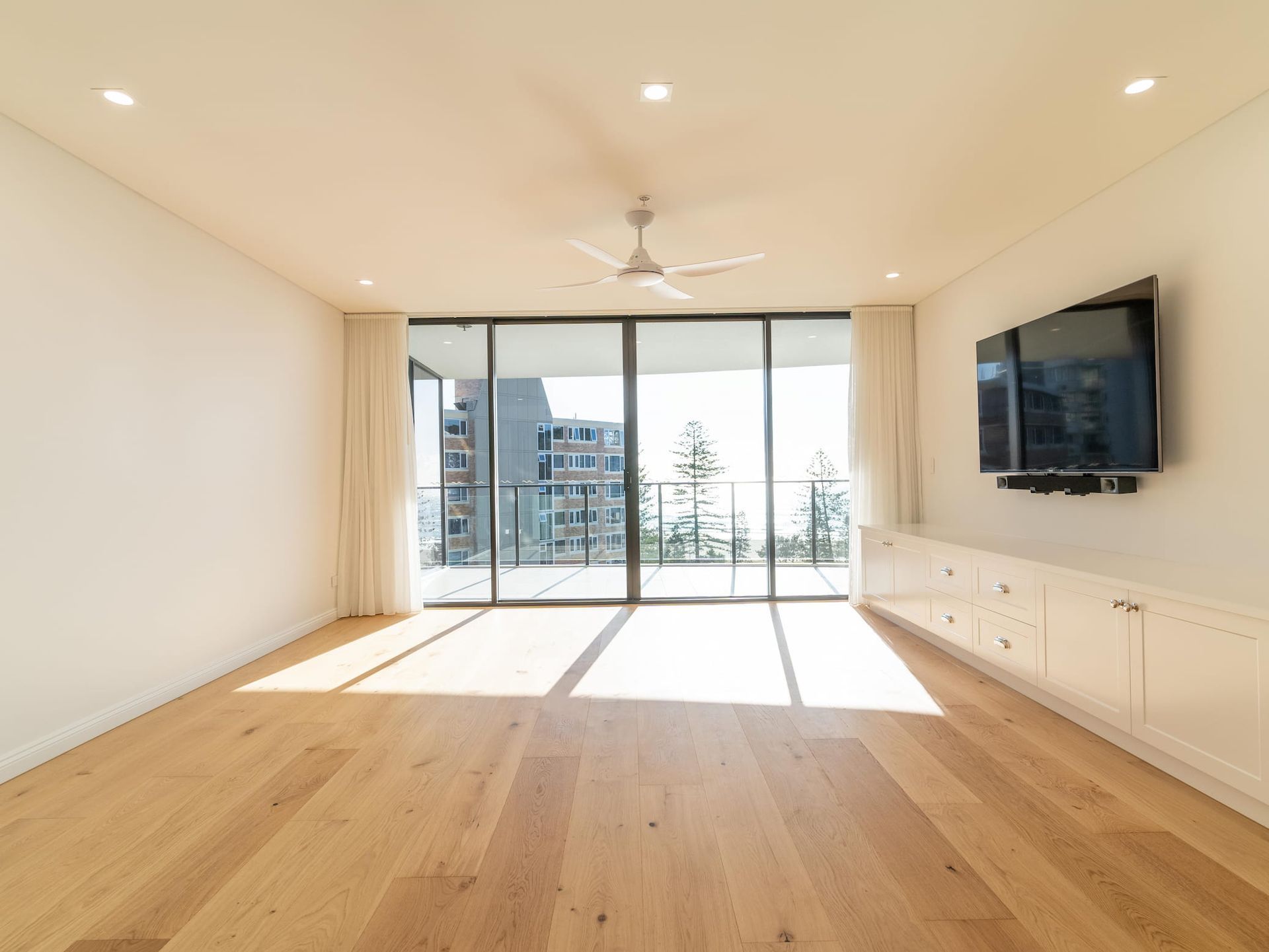 Empty living room with wood floors, large window, and built-in white cabinets.