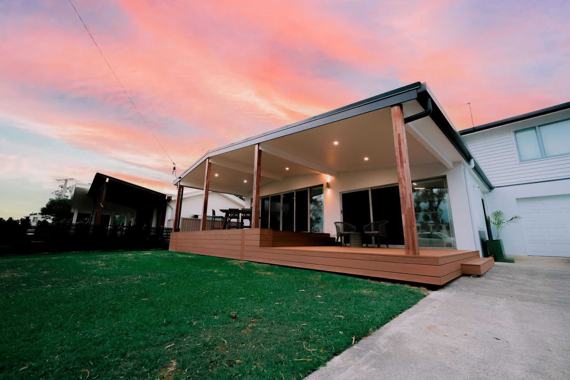 Modern house with a covered porch, wooden deck, and green lawn at sunset.