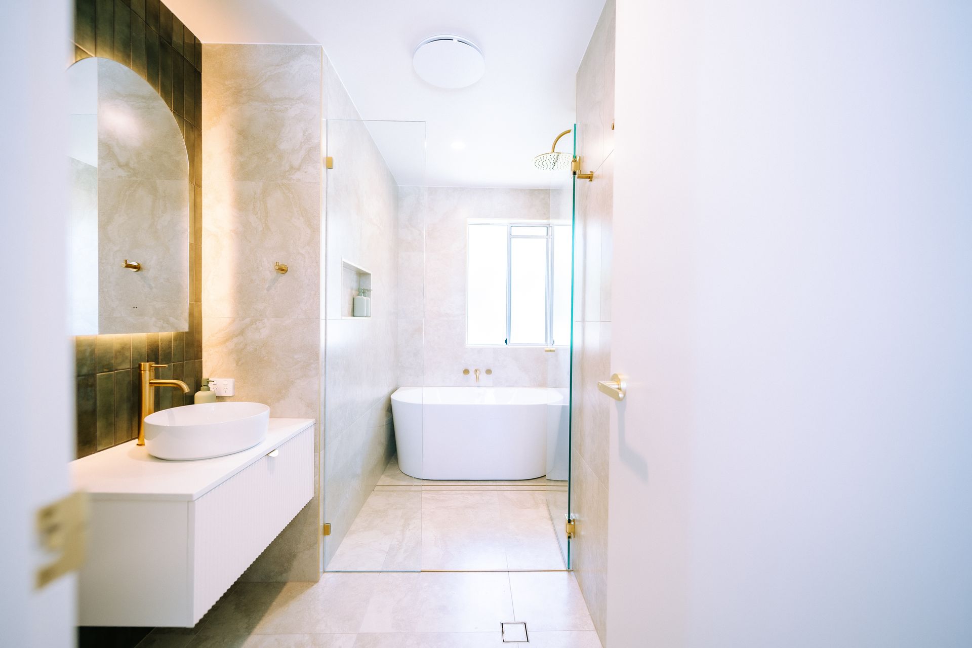 Modern, bright bathroom with white fixtures and gold accents, including a freestanding tub.