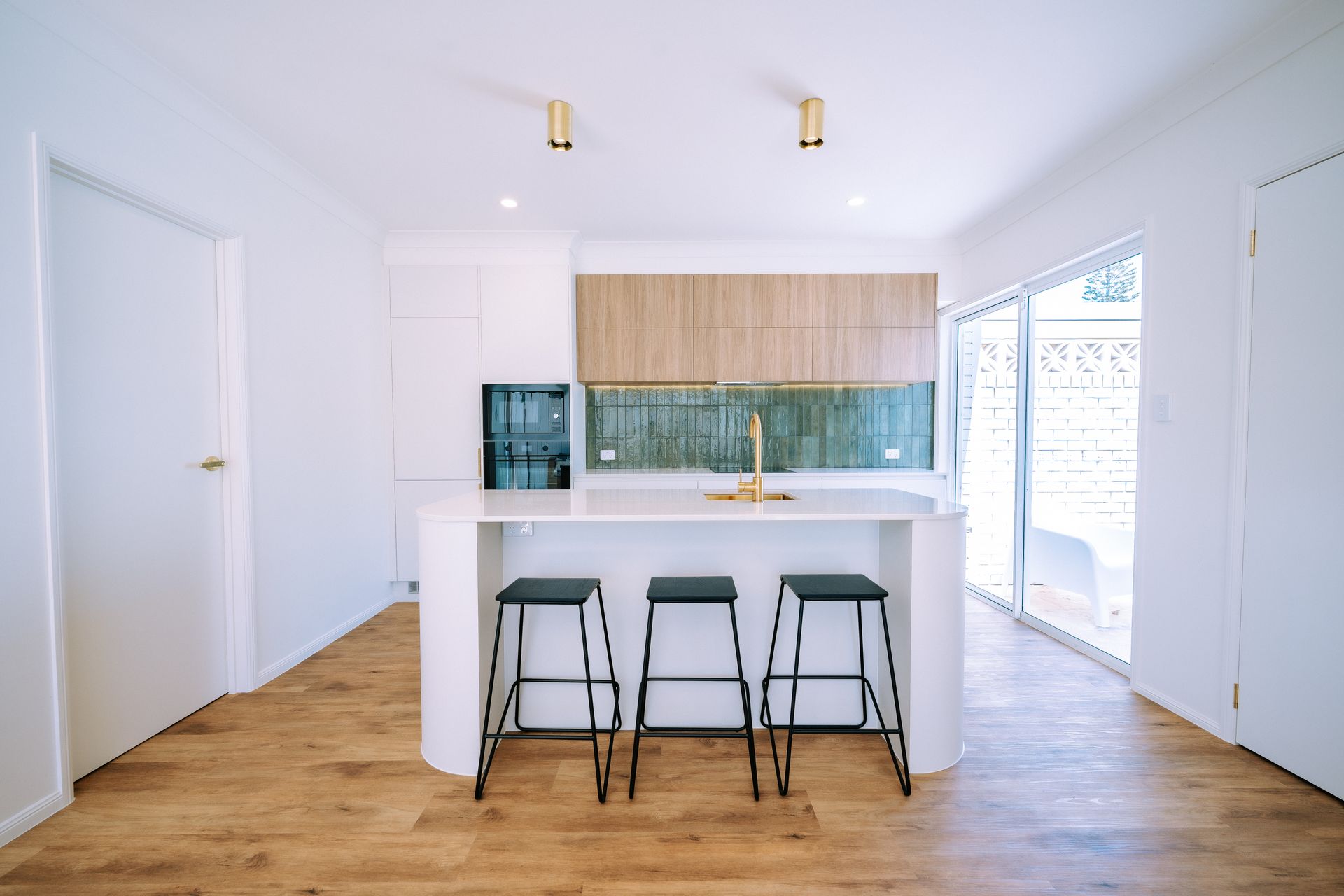 Bright kitchen with wood-look floor, white island with stools, wood cabinets, and glass backsplash.