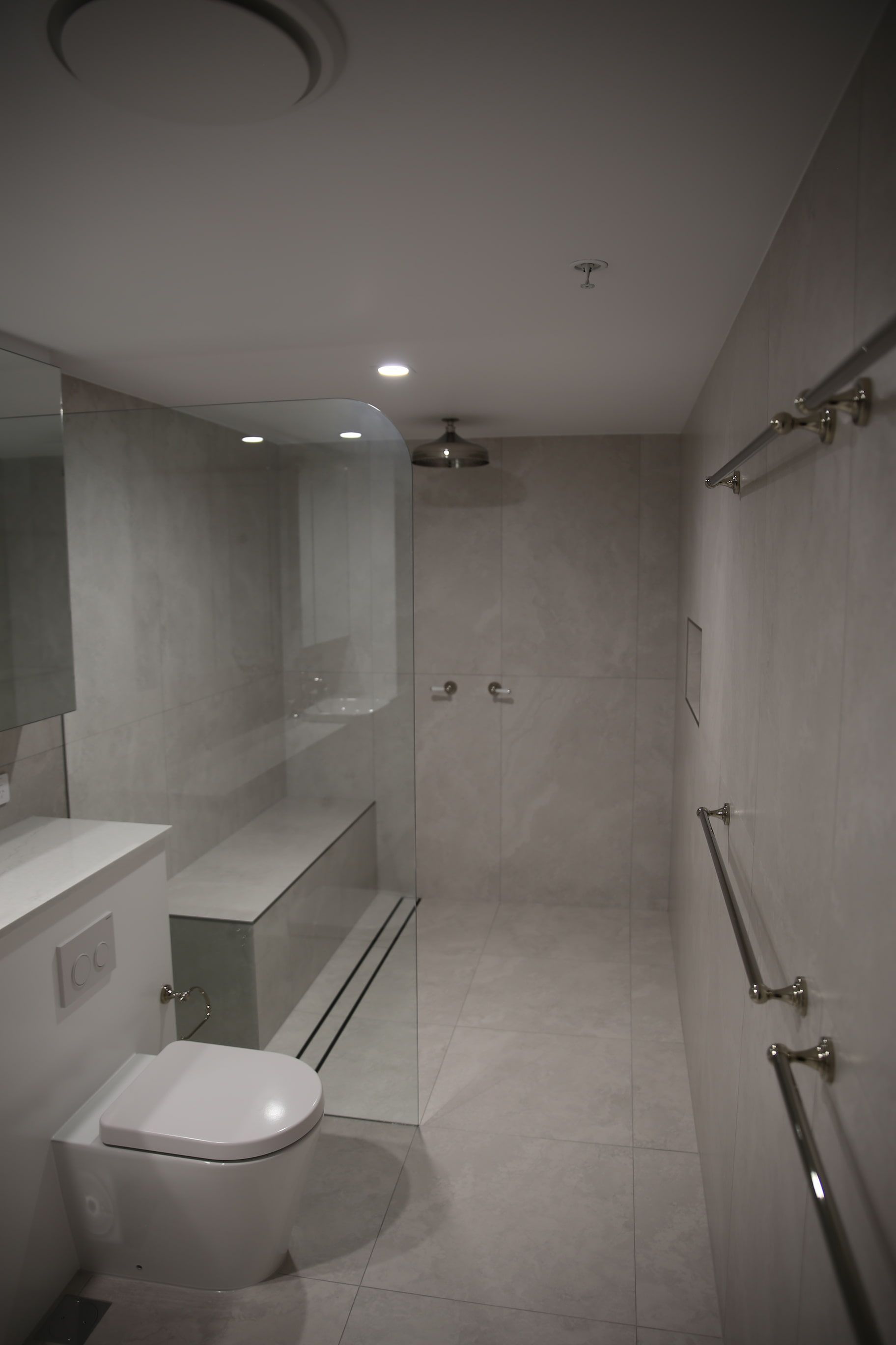 Modern, gray-tiled bathroom with walk-in shower, toilet, and grab bars.