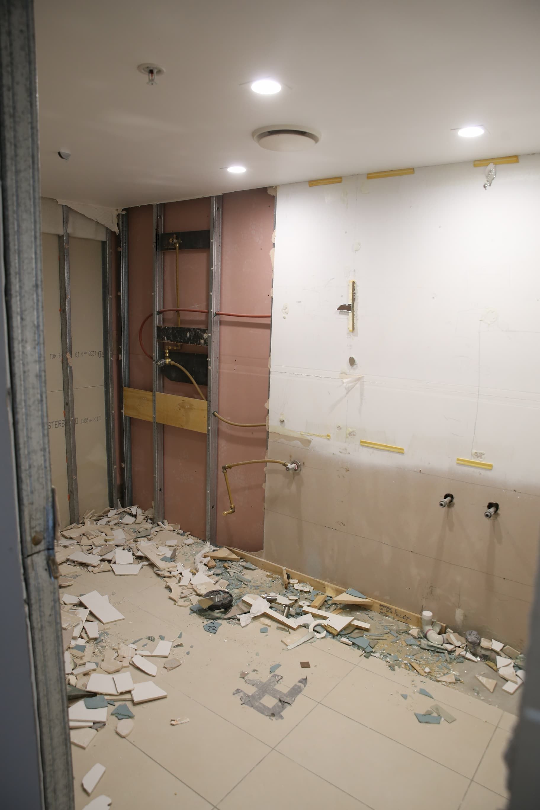 Bathroom renovation in progress; walls torn open, debris on floor, exposed studs and pipes.