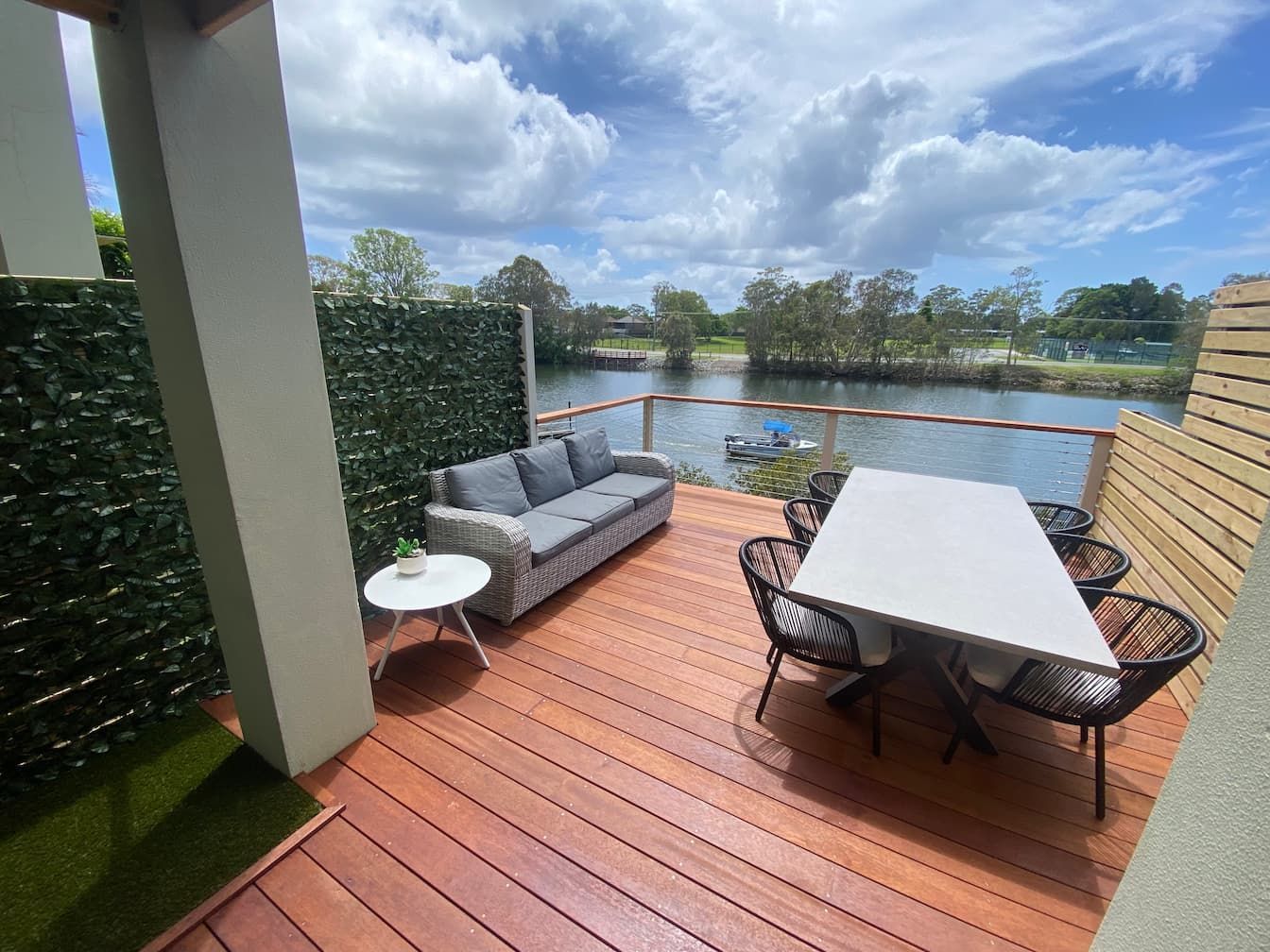 Outdoor patio with sofa, dining table, and water view under cloudy sky.