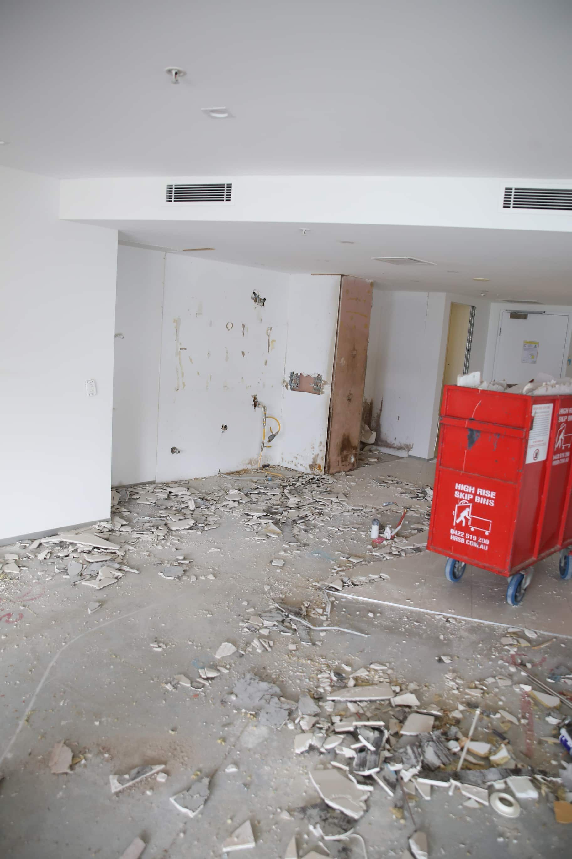 Room under construction, debris on floor, walls damaged, red utility cart on wheels.