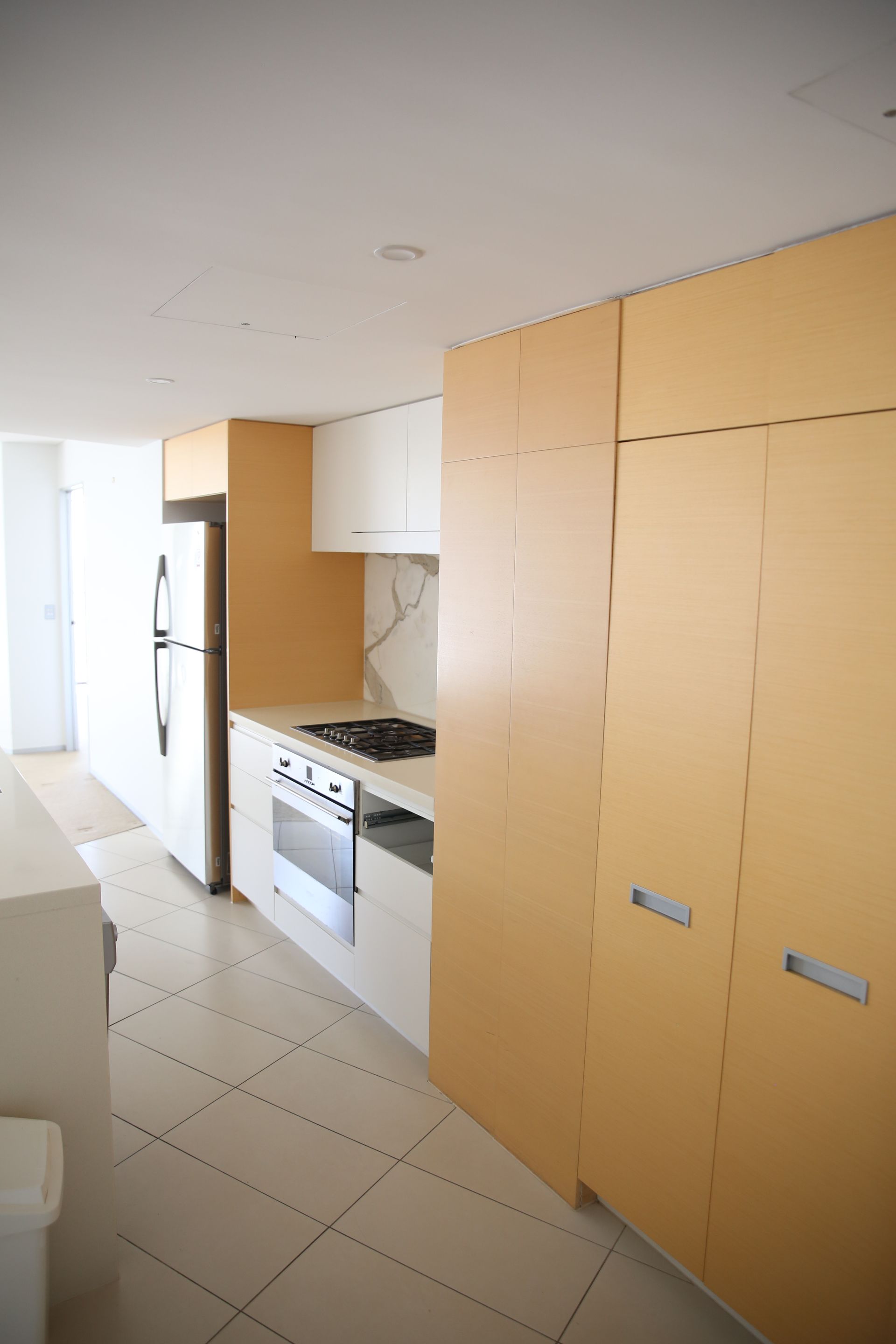 Modern kitchen with light wood and white cabinetry, stainless steel appliances, and tiled floor.