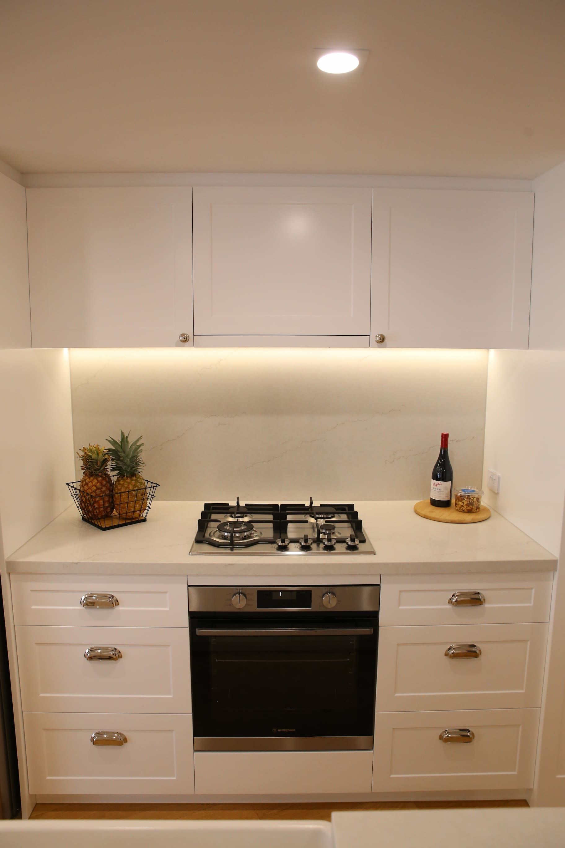 White kitchen with stove, oven, cabinets, and counter space.  Pineapples and wine bottle on counter.