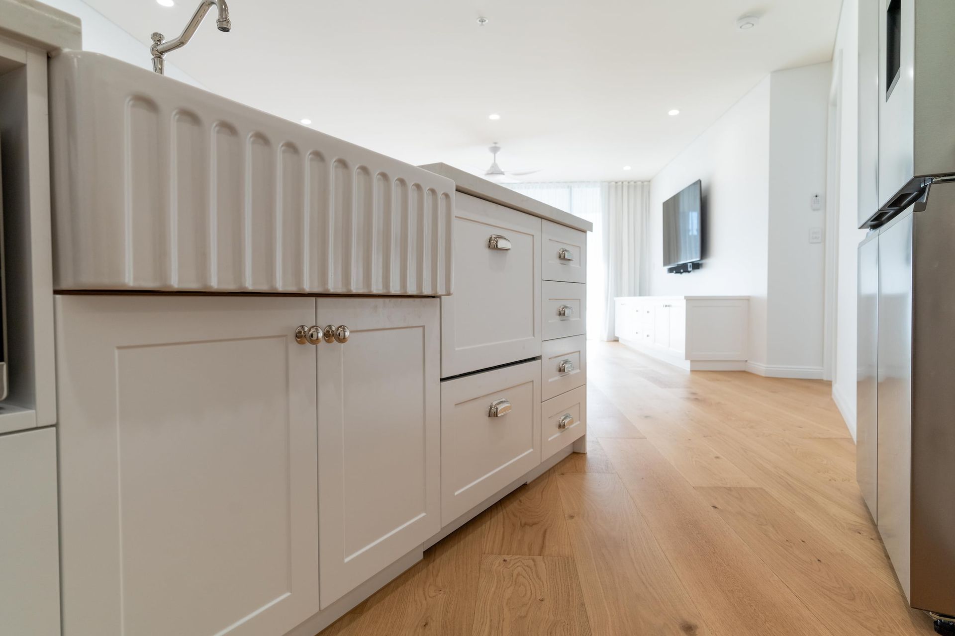 White kitchen island with a farmhouse sink, light wood floors, and a modern kitchen.