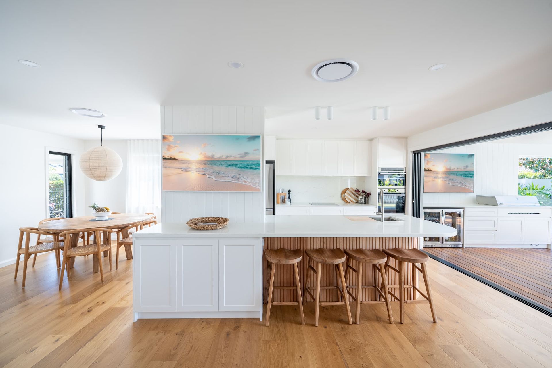Open-plan kitchen with white cabinetry, wooden island, and dining table, all on a light wood floor.