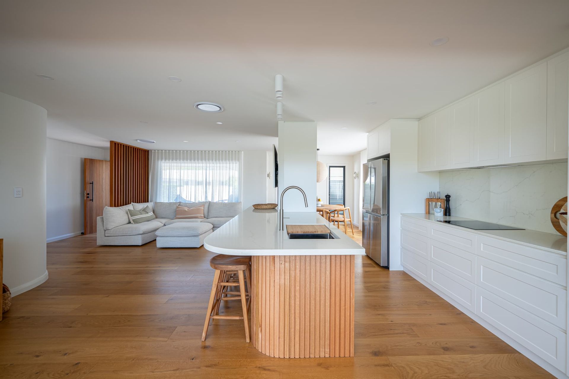 Open-plan kitchen with wooden floors, white cabinetry, island with wood paneling, and a living area with a couch.