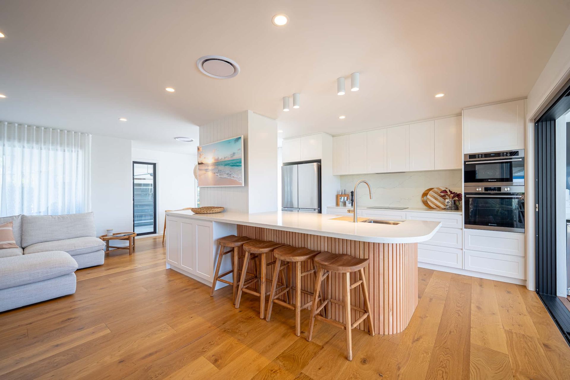 Modern kitchen with wooden floors, island with stools, and white cabinetry.
