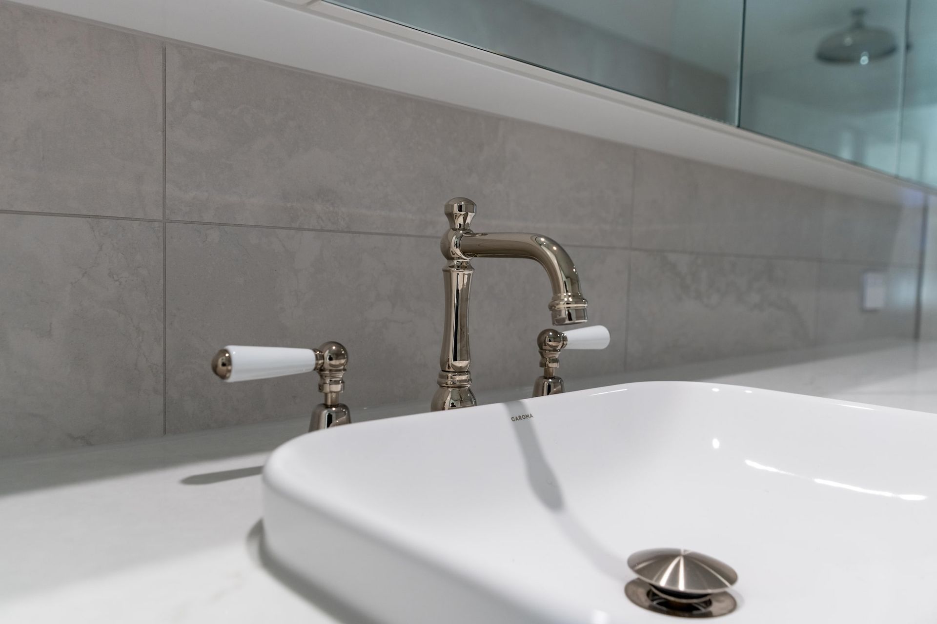 Bathroom sink with chrome faucet and white porcelain basin, set against gray tiled wall.