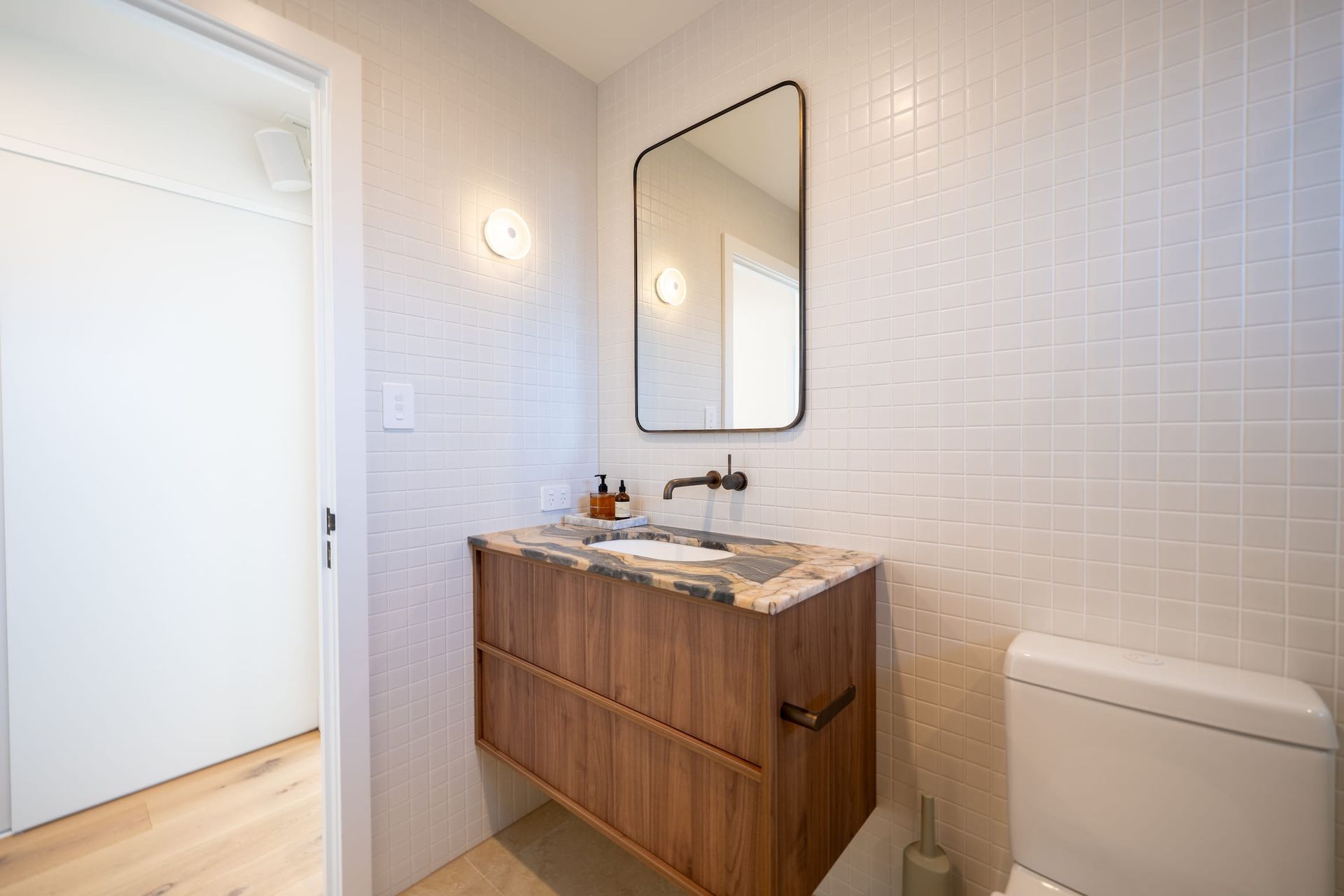 Bathroom with floating wood vanity, marble countertop, square tile walls, and a black-framed mirror.