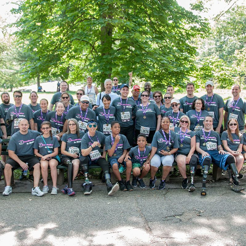 A large group of amputees and staff are posing for a picture in a park.