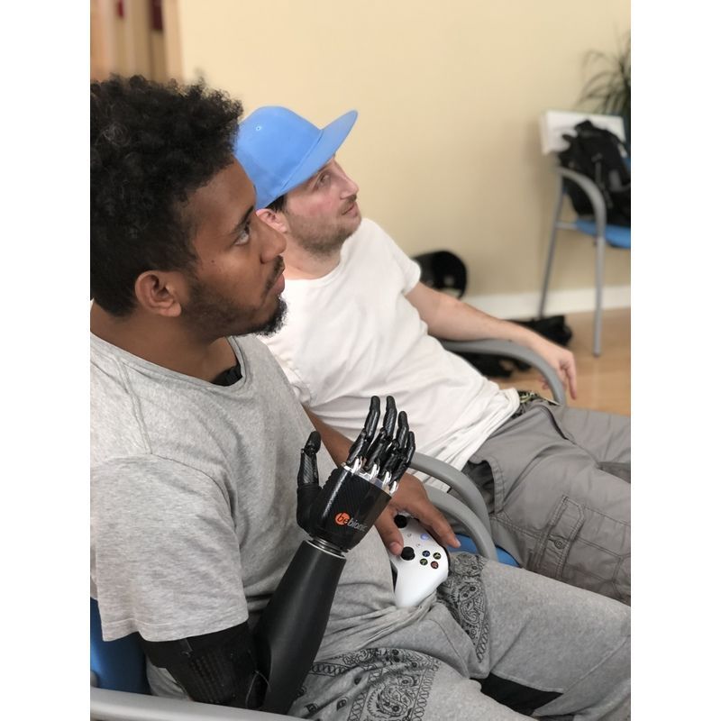A man with a prosthetic arm is sitting next to another man