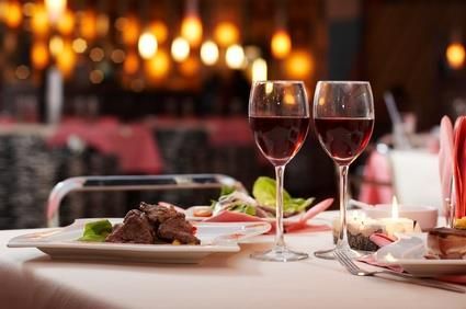 Two glasses of red wine are on a table with plates of food.